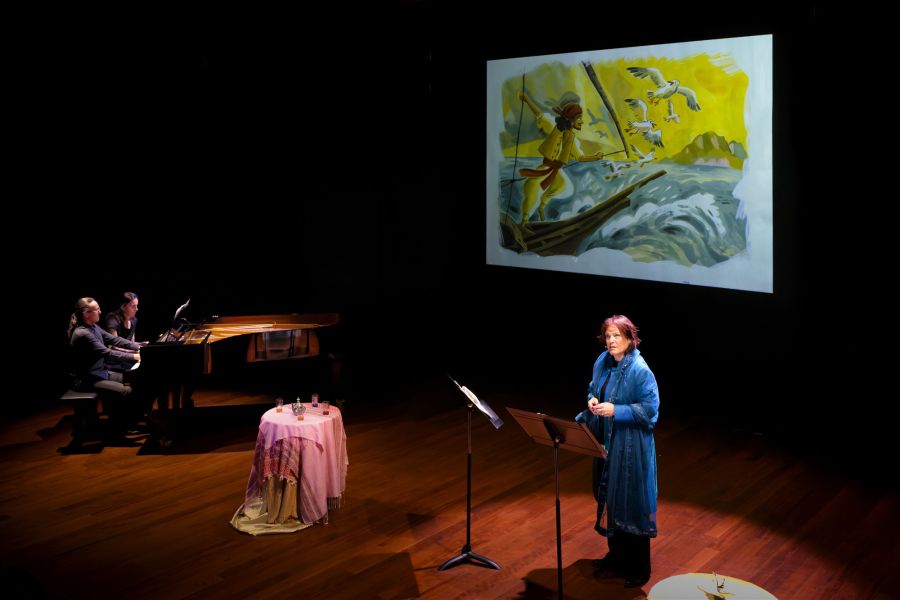 Sur scène, la récitante devant son pupitre, les deux pianistes au piano et une illustration projetée sur grand écran